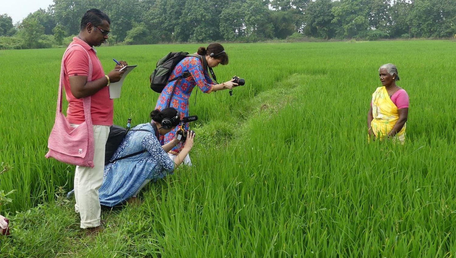 Three people filming a women in a green field